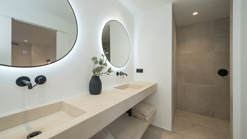 Salle de bains minimaliste avec deux miroirs ronds rétroéclairés, double vasque en pierre et robinetterie noir mat.