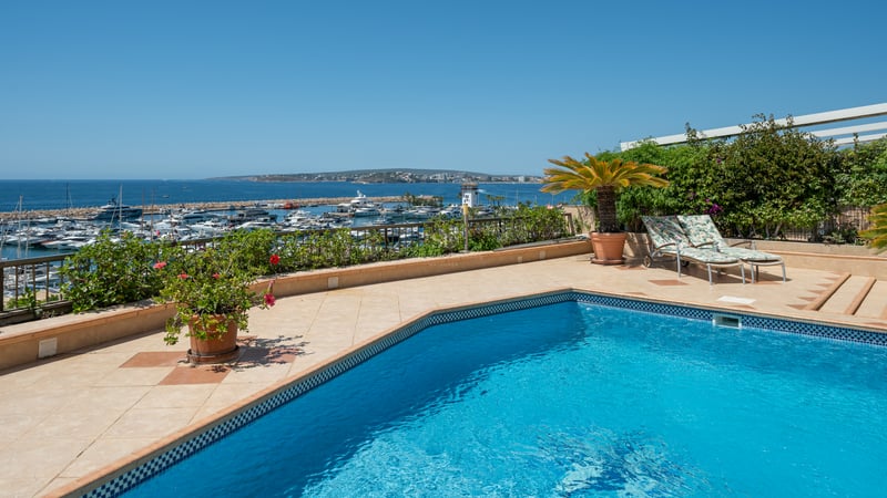 Piscine sur une terrasse en carrelage surplombant un port de plaisance de luxe et la mer Méditerranée.
