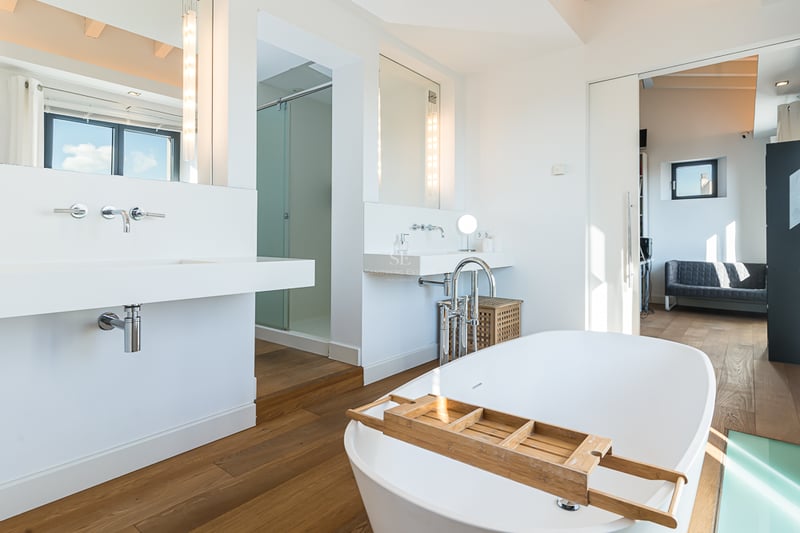 Salle de bain principale lumineuse avec baignoire îlot blanche, parquet et lavabos suspendus modernes.