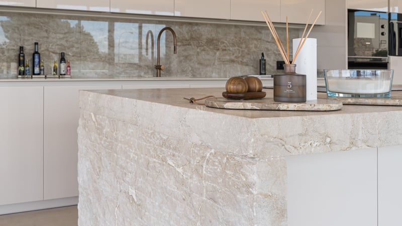 Gros plan d'un îlot de cuisine en pierre naturelle avec robinetterie en cuivre et décoration minimaliste.
