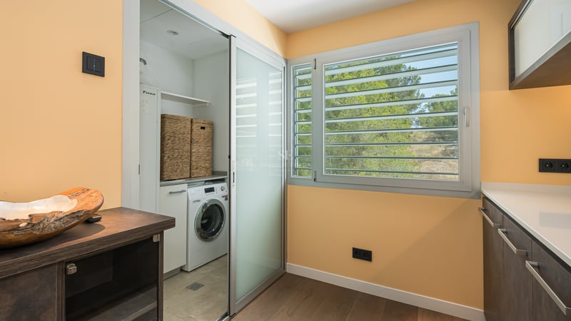 Buanderie moderne avec lave-linge dissimulé derrière une porte en verre dépoli et fenêtre à persiennes.