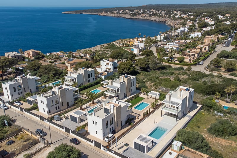 Vue par drone de villas blanches modernes avec piscines privées sur une côte rocheuse au bord de la mer bleue.