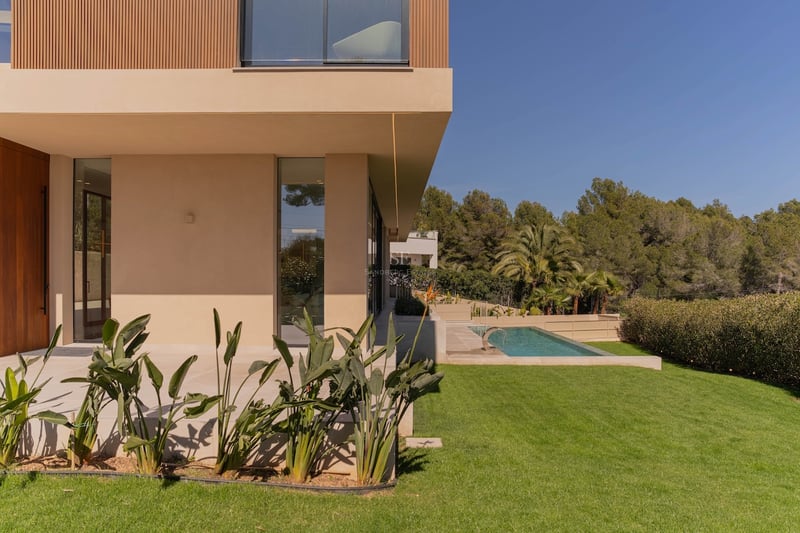 Profil latéral d'une villa moderne à deux étages avec murs couleur sable, accents en bois, pelouse et piscine.