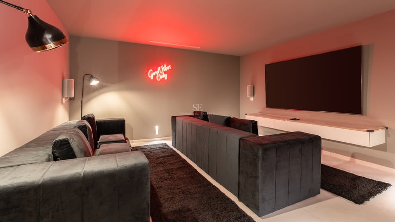 Salle de cinéma avec canapés en velours gris, grand écran plat et éclairage néon rouge.