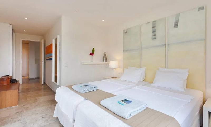 Chambre lumineuse avec lits jumeaux, triptyque artistique, sol en travertin et murs blancs dans une villa moderne.
