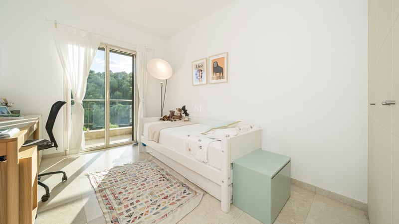Chambre blanche avec lit simple, bureau, accès terrasse et tapis géométrique.