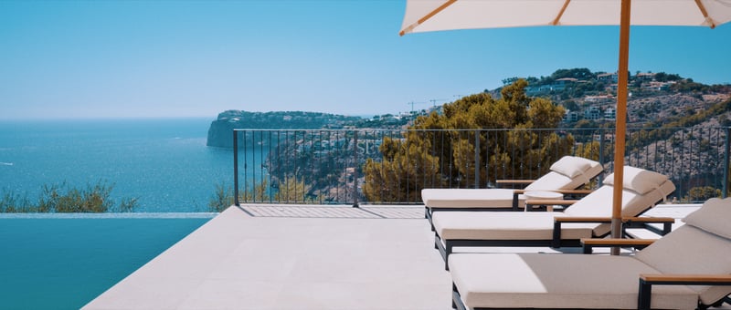 Terrasse de luxe avec chaises longues blanches et parasol à côté d'une piscine à débordement surplombant la mer.