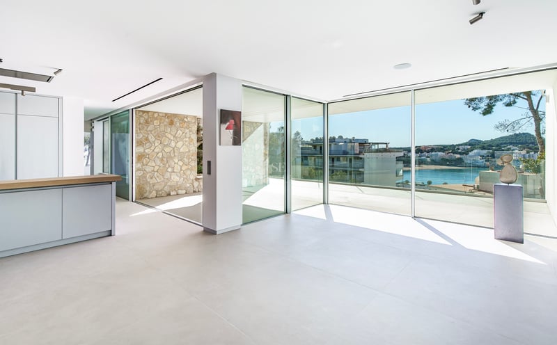 Espace de vie moderne et lumineux avec baies vitrées donnant sur une baie méditerranéenne et mur en pierre.