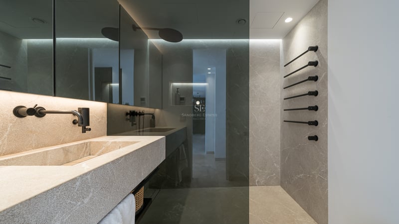 Salle de bain moderne avec lavabo en pierre, robinetterie noir mat et murs en pierre avec paroi de douche en verre.