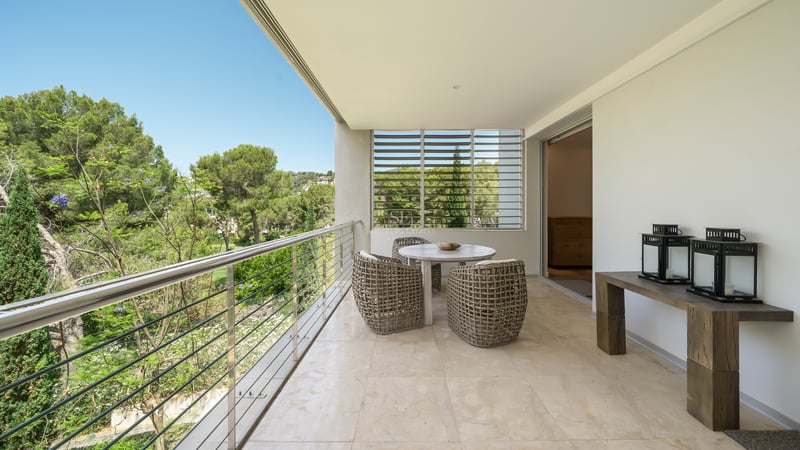 Terrasse spacieuse avec sol en marbre, meubles en osier, garde-corps en acier et vue sur les pins.