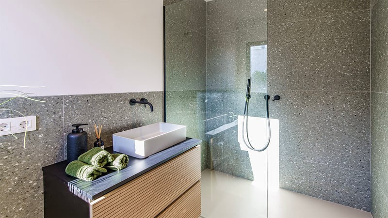 Salle de bain moderne avec carrelage gris moucheté, vasque blanche sur meuble en bois et douche à l'italienne.