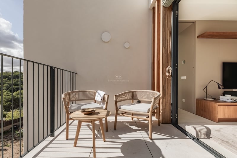 Balcon ensoleillé avec fauteuils design tressés et table en bois surplombant une forêt verdoyante.