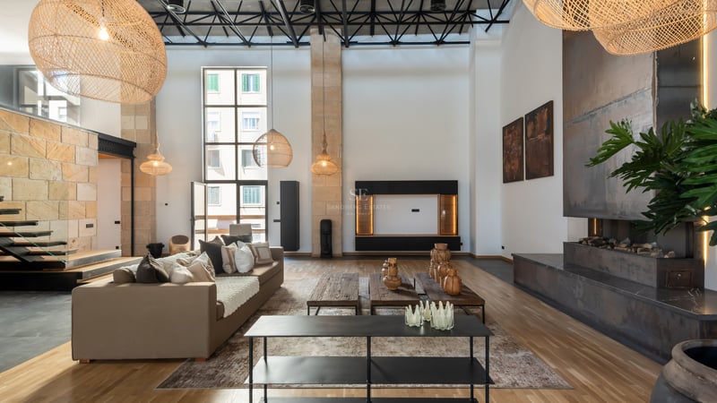Salon moderne avec plafonds double hauteur, canapés beige, cheminée en métal et grandes suspensions en osier.