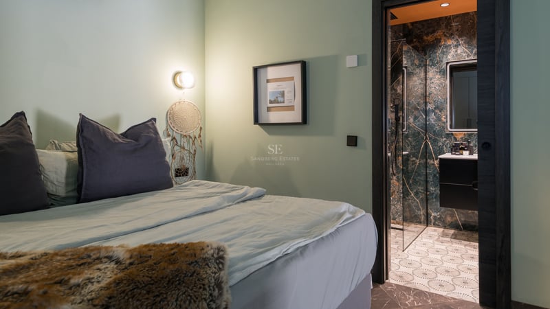 Chambre moderne aux murs vert sauge avec vue sur une salle de bain en marbre vert foncé.