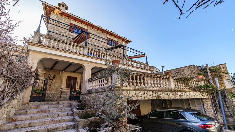 Maison en pierre à plusieurs niveaux avec balustrades en fer forgé et escaliers en pierre sous un ciel bleu.