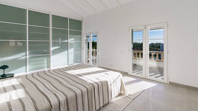 Chambre lumineuse avec lit rayé, plafonds voûtés blancs, placards en verre dépoli et accès à un balcon.