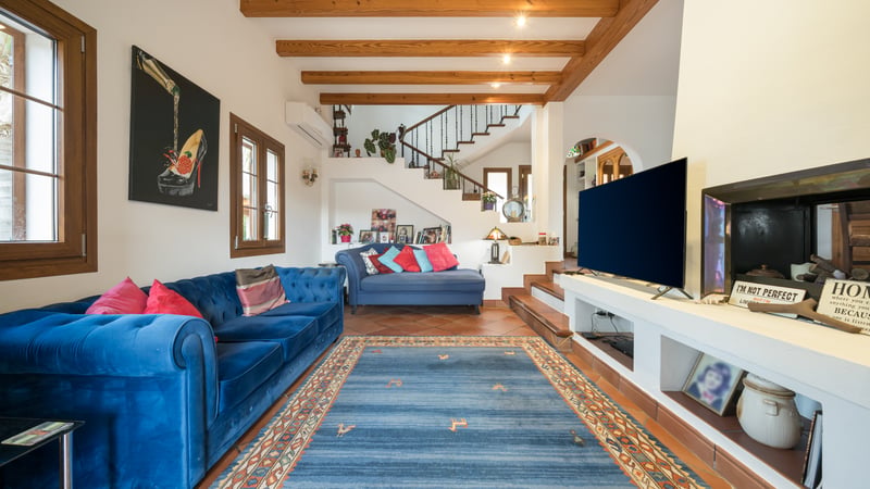 Salon spacieux avec canapés en velours bleu, poutres en bois apparentes au plafond et sol en terre cuite traditionnelle.