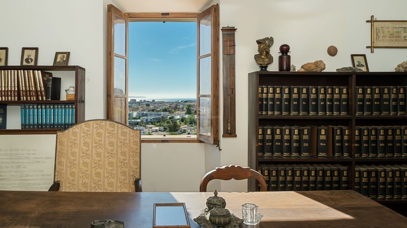 Bureau traditionnel en bois avec bibliothèques et fenêtre ouverte donnant sur la mer et la ville.