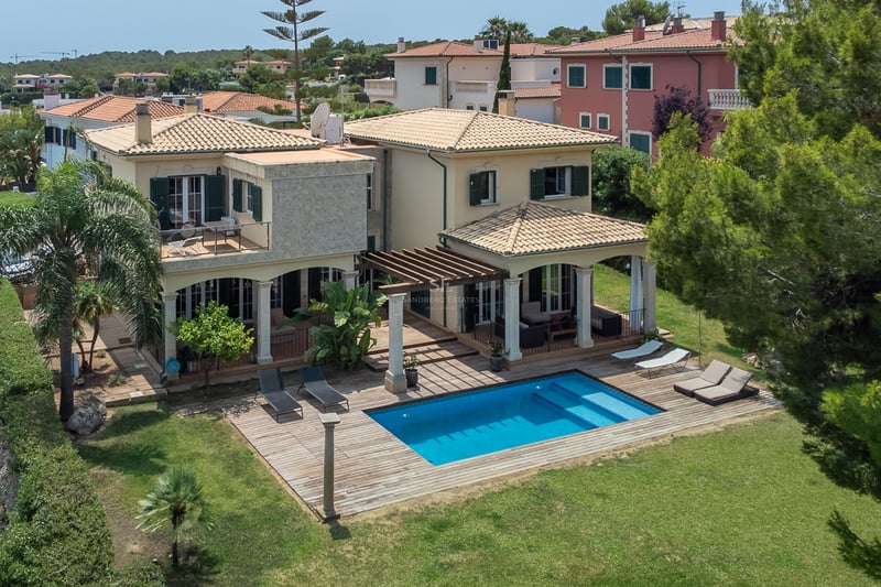 Vue surélevée d'une villa crème avec piscine, terrasse en bois et jardin verdoyant sous le soleil.