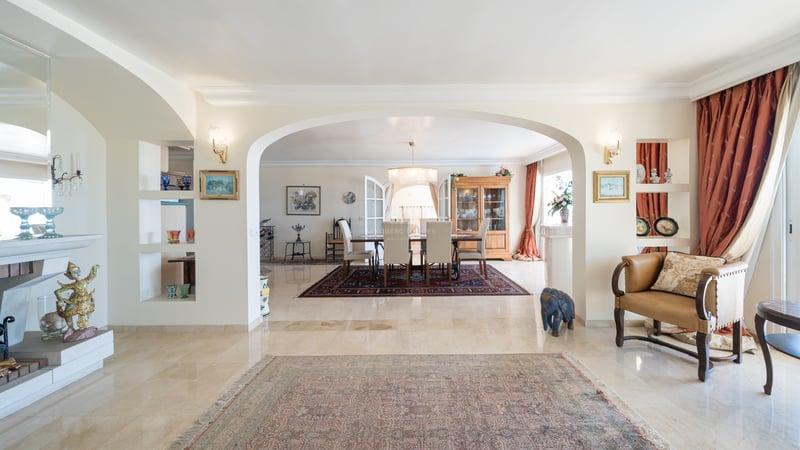 Vaste espace de vie avec sols en marbre et une arche encadrant une salle à manger formelle avec lustre et tapis classiques.
