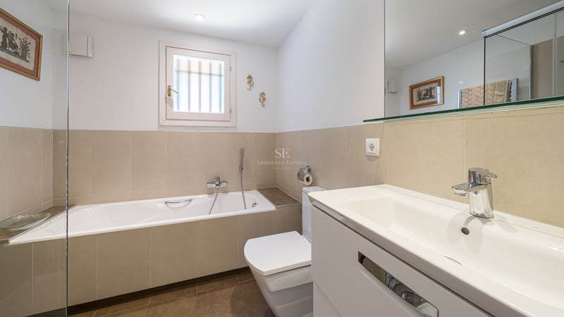 Salle de bain contemporaine avec baignoire encastrée, meuble vasque blanc avec miroir et carrelage beige.