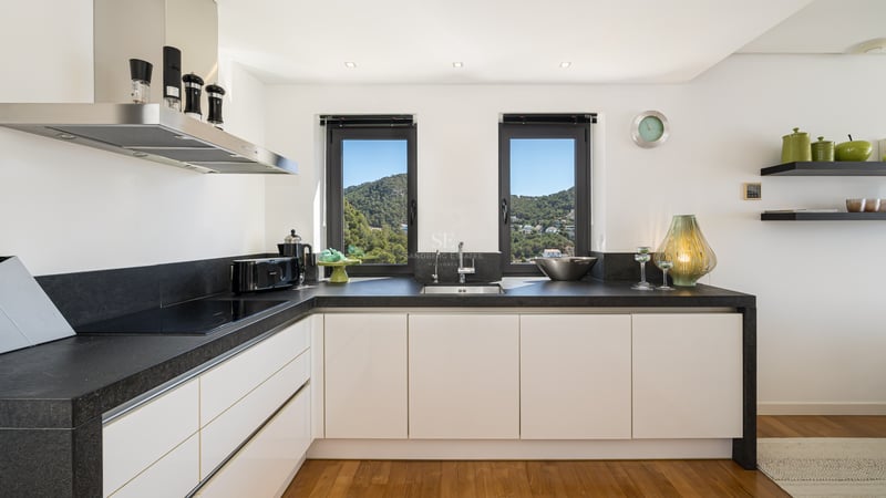 Cuisine blanche contemporaine avec plans de travail en pierre sombre, parquet et fenêtres sur la montagne.