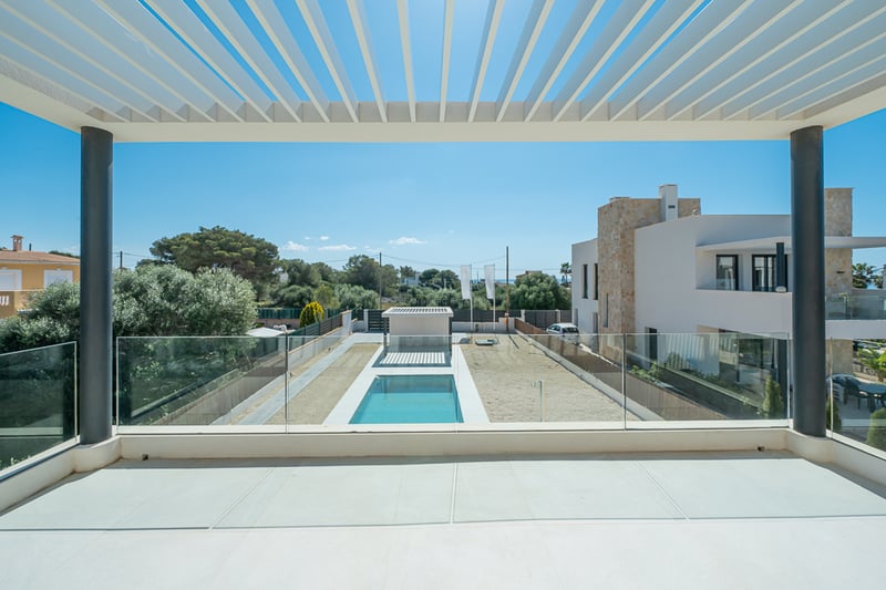 Vue depuis un balcon moderne avec pergola blanche et garde-corps en verre donnant sur une piscine et un jardin.