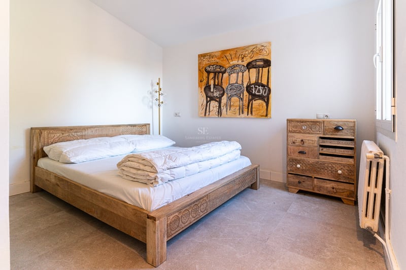 Chambre lumineuse avec lit en bois sculpté, commode assortie, tableau abstrait et sol en pierre naturelle.