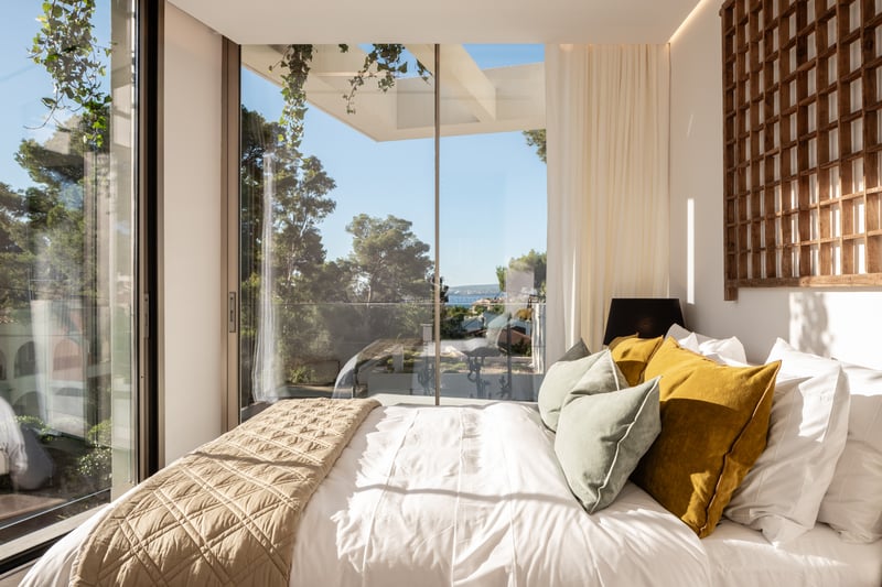 Chambre moderne avec baies vitrées, tête de lit en bois et vue sur les pins et la Méditerranée.
