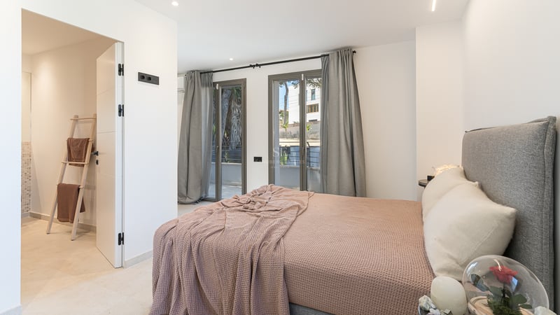 Chambre contemporaine avec lit gris, jeté de lit mauve, baies vitrées et accès à une salle de bain attenante.