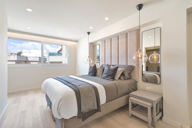 Chambre contemporaine avec tête de lit capitonnée, suspensions en verre et parquet en bois clair.