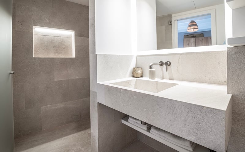 Salle de bain moderne en pierre avec vasque intégrée, robinet mural et niche murale éclairée.