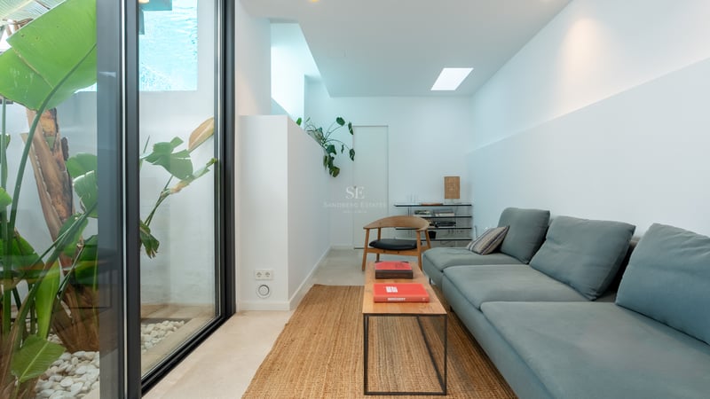 Salon moderne avec canapé bleu, table basse en bois, tapis en jute et baie vitrée donnant sur des plantes tropicales.