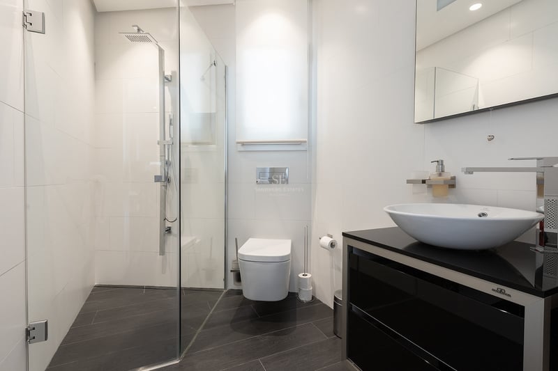 Salle de bain contemporaine avec carrelage blanc, douche en verre, toilettes suspendues et vasque sur meuble noir.
