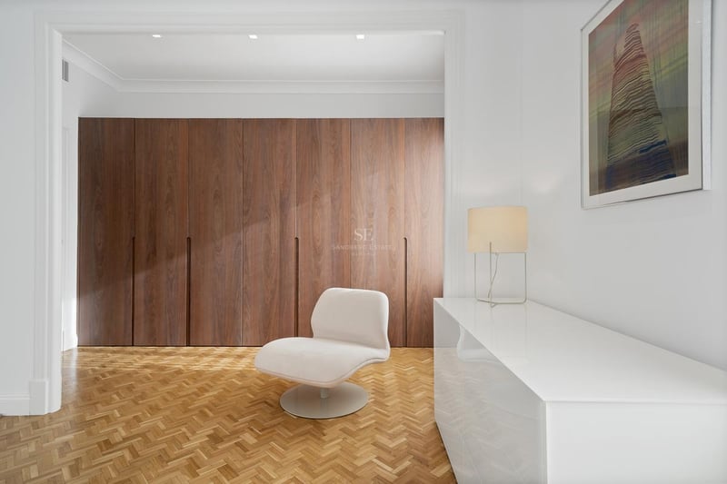 Espace dressing minimaliste avec placards en bois, parquet à chevrons et fauteuil design blanc.