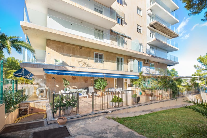 Immeuble d'appartements avec parement en pierre, balcons en verre et grande terrasse au rez-de-chaussée.