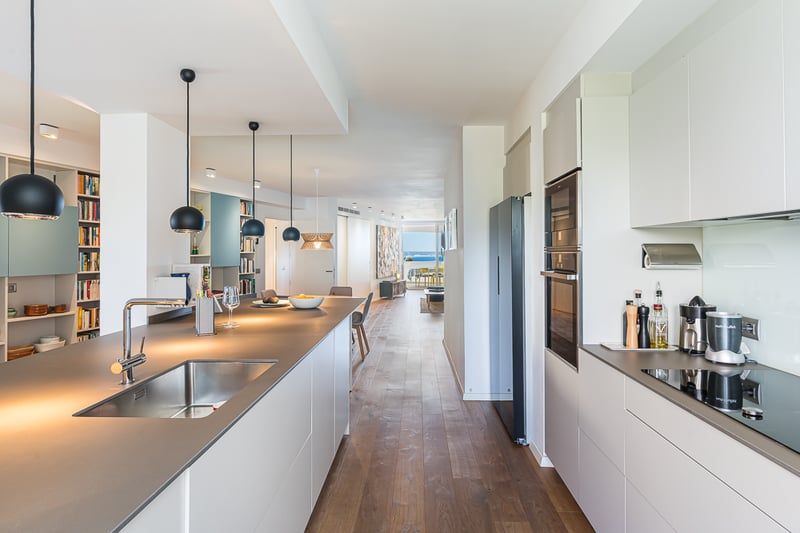 Grand balcon avec vue sur la mer. Balustrade en verre, plancher en bois et mobilier moderne. Éclairage d'ambiance et ciel bleu.