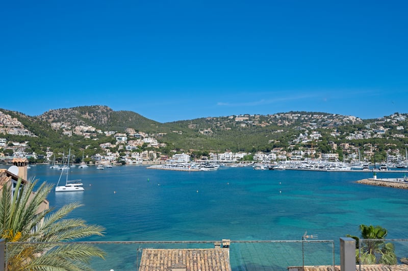 Vue en plongée d'un port méditerranéen turquoise rempli de yachts, entouré de collines vertes et de villas blanches.