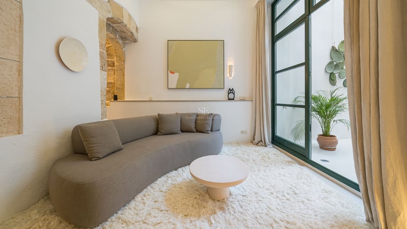 Canapé incurvé taupe sur tapis blanc dans une pièce lumineuse avec arche en pierre et portes vitrées sur patio.