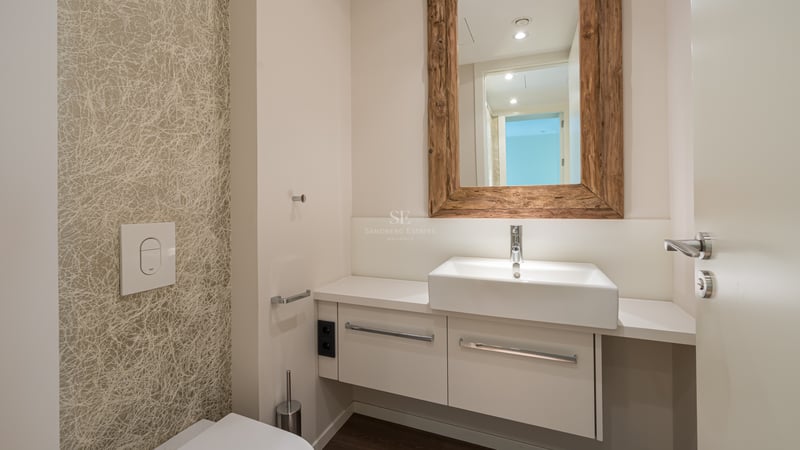 Salle de bain moderne avec vanité blanche, robinetterie chromée et grand miroir à cadre en bois rustique sur papier peint.
