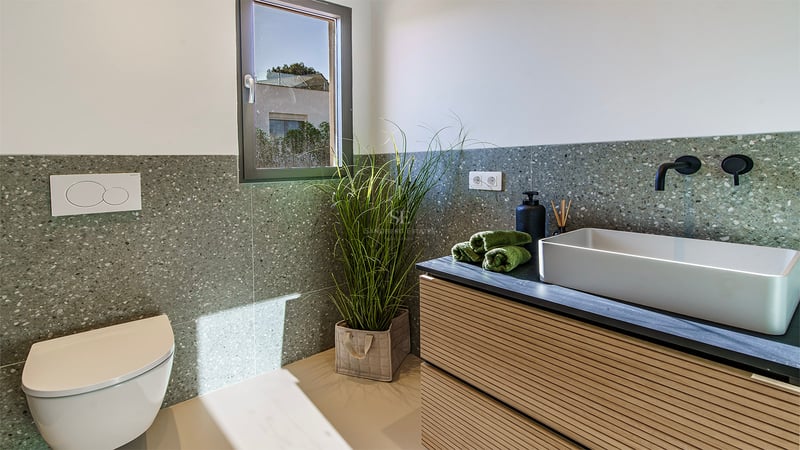 Salle de bain minimaliste avec vasque à poser, robinetterie noire, WC suspendu et murs en terrazzo vert.
