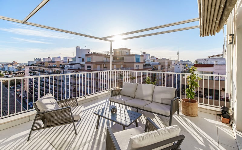 Terrasse ensoleillée avec mobilier gris moderne, balustrades blanches et vue imprenable sur la ville.