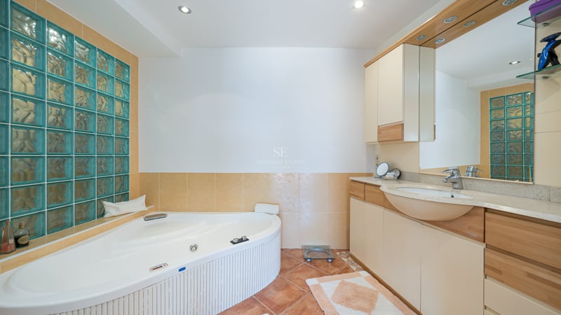 Vue d'une salle de bains avec baignoire balnéo d'angle, briques de verre turquoise et meuble vasque en bois.