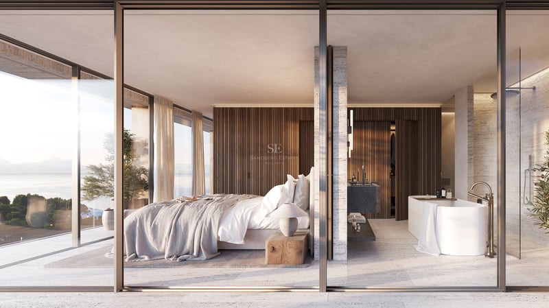 Chambre principale moderne et salle de bain attenante séparées par du verre, avec vue sur la mer et boiseries.