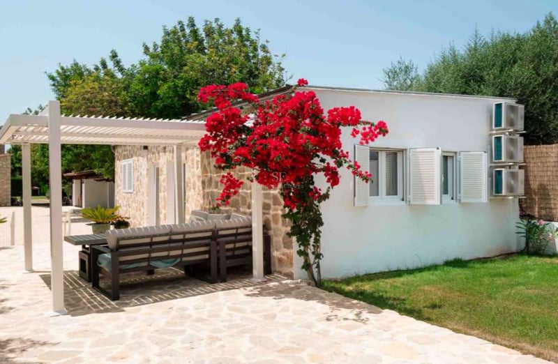 Bâtiment blanc avec façade en pierre, bougainvillier rouge et pergola moderne sur une terrasse aménagée.