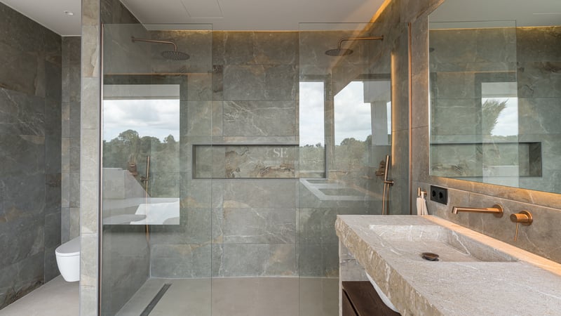 Salle de bain contemporaine avec carrelage en pierre grise, paroi en verre et vasque en pierre naturelle.