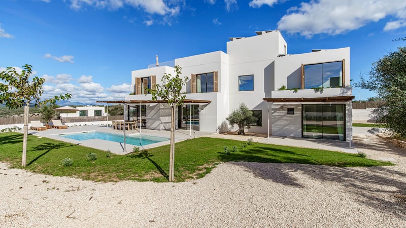Villa moderne blanche à deux étages avec piscine rectangulaire, pergolas en bois et jardin sous un ciel bleu.