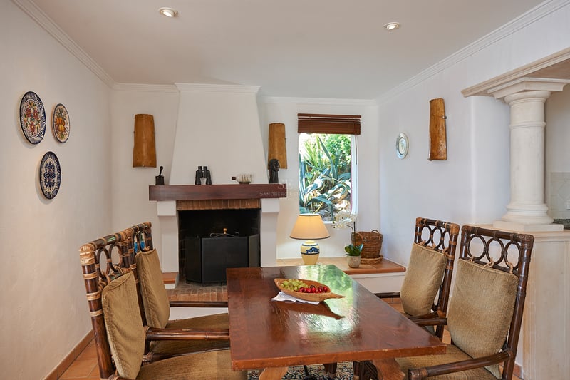 Salle à manger avec table en bois, chaises en bambou, cheminée blanche et assiettes décoratives au mur.