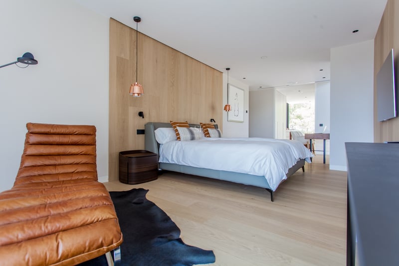 Chambre principale contemporaine avec boiseries, chaise longue en cuir fauve et suspensions en cuivre.