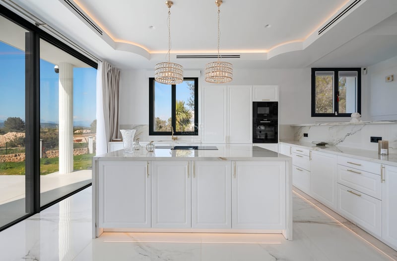 Cuisine moderne lumineuse avec grand îlot en marbre, finitions dorées et baies vitrées donnant sur le jardin.